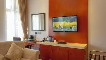A hotel room with a sofa, a desk with a computer and telephone, a television mounted on the wall, and a window with curtains.