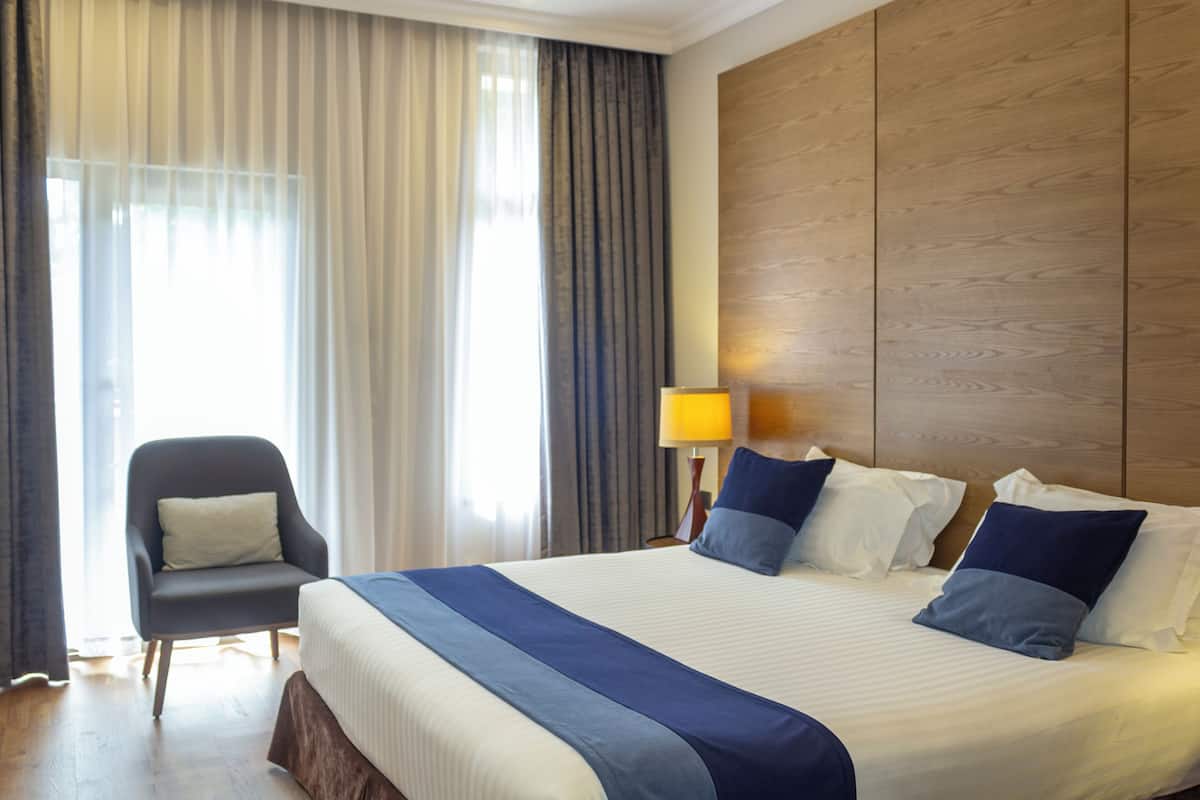 A hotel room with a large bed, a chair, a lamp, and a wooden headboard.