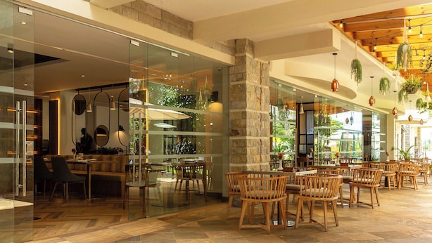 A spacious indoor area with a mix of seating arrangements, including wooden chairs and tables, and a stone pillar. - Alba Hotel Meru (Meru)