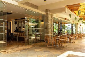 A spacious indoor area with a mix of seating arrangements, including wooden chairs and tables, and a stone pillar. - Alba Hotel Meru (Meru)