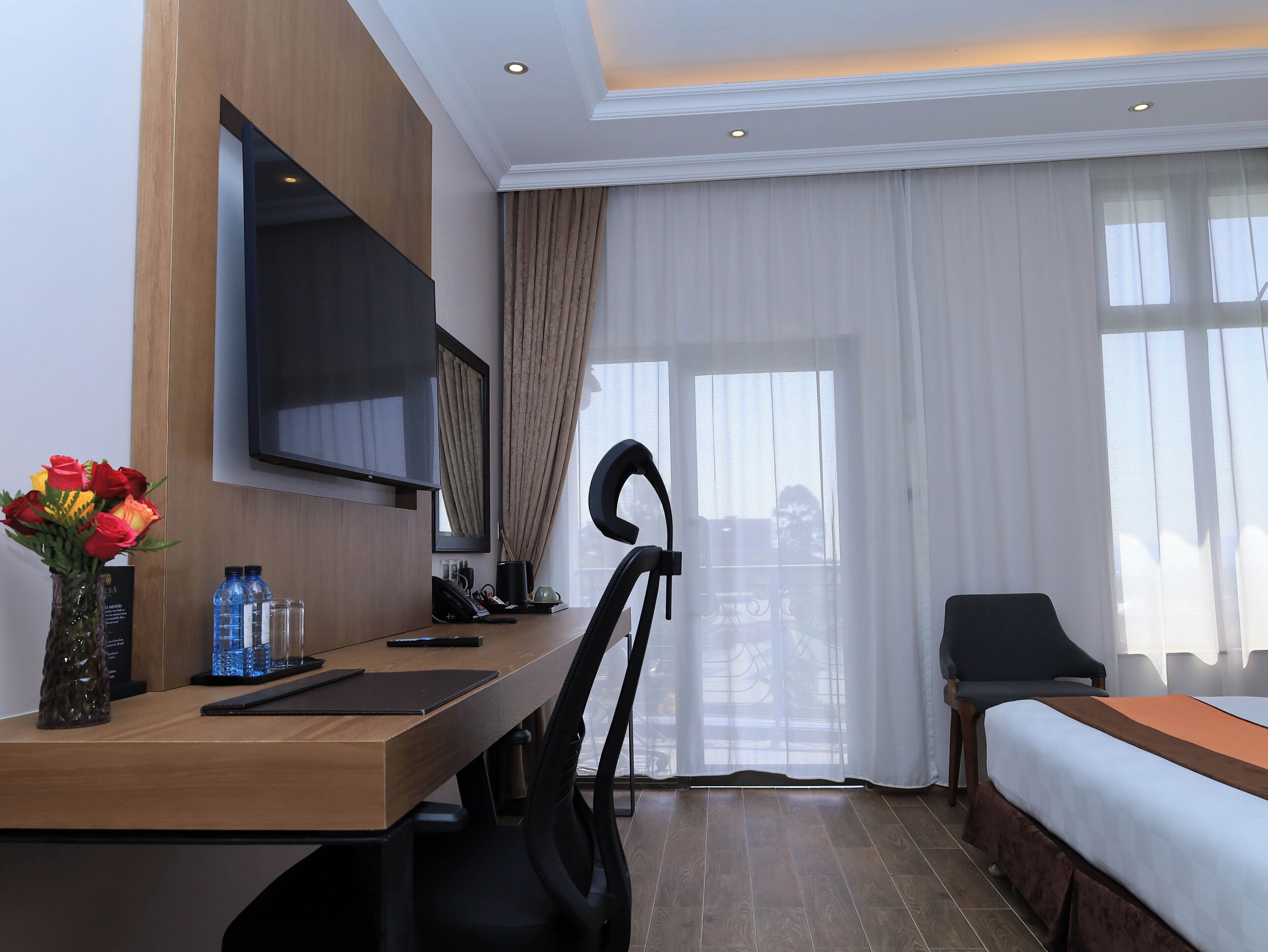 Una habitación de hotel con cama, escritorio con silla, televisor y ventana con cortinas.