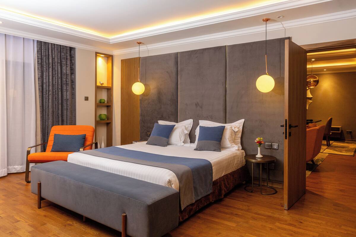 A modern hotel room with a large bed, a seating area with a chair, and a small table with a vase.