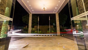 A hotel entrance with a modern design, featuring a central chandelier, a glass facade, and a well-lit pathway leading to the entrance. - Alba Hotel Meru (Meru)