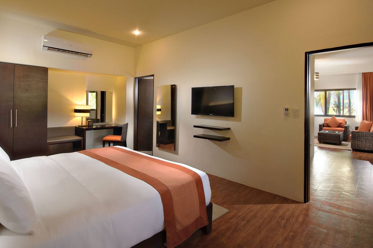 Habitación de hotel con cama, escritorio, televisor y zona de estar con vistas.