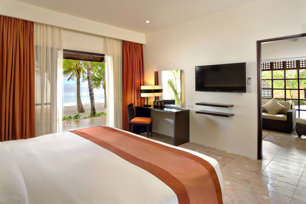 Habitación de hotel con cama, escritorio, televisión y vista a la playa.