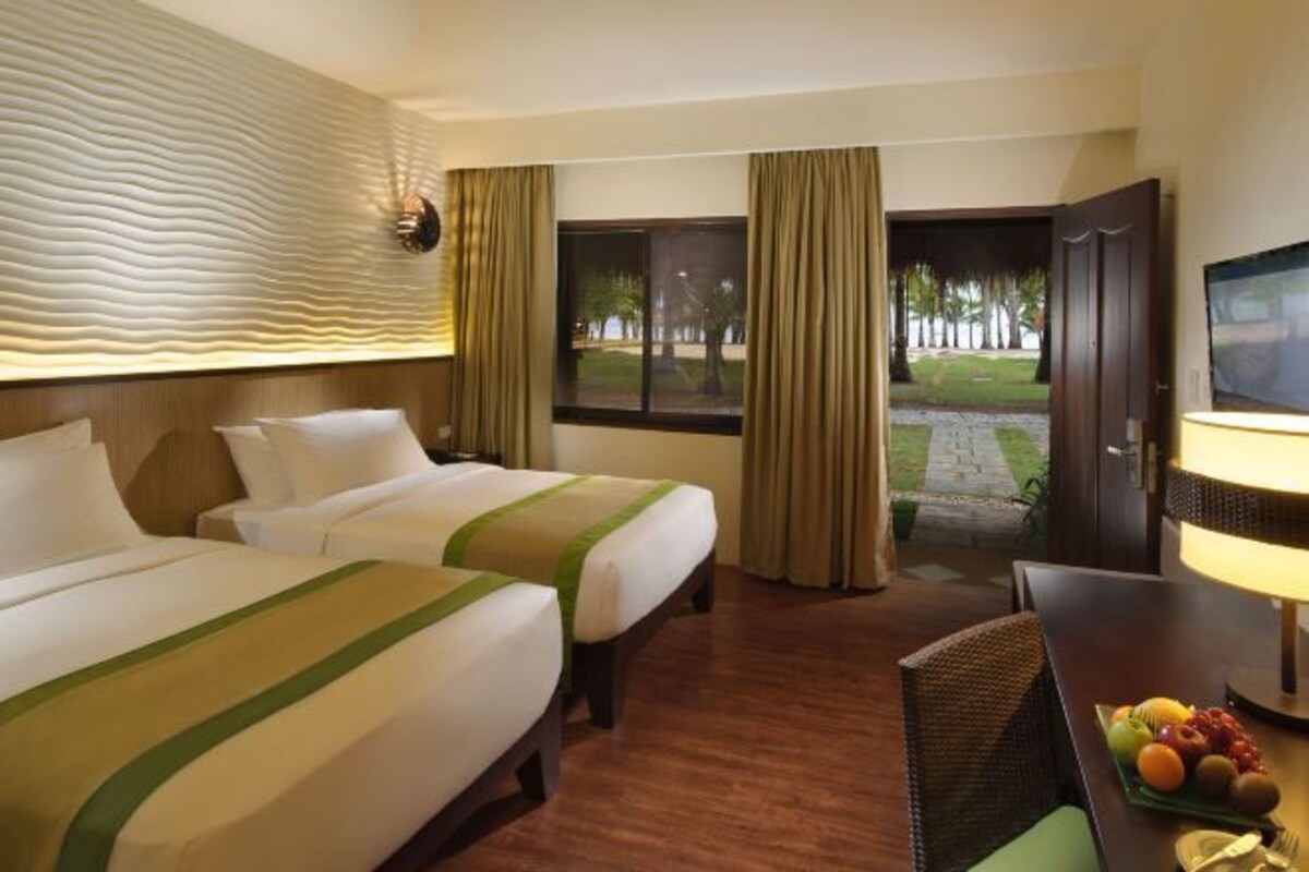 Una habitación de hotel con dos camas, una televisión, una mesa de comedor con fruta y vistas a un jardín por la ventana.