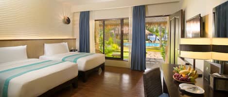 A hotel room with two beds, a dining table with fruit, a TV, and a view of a pool and garden.