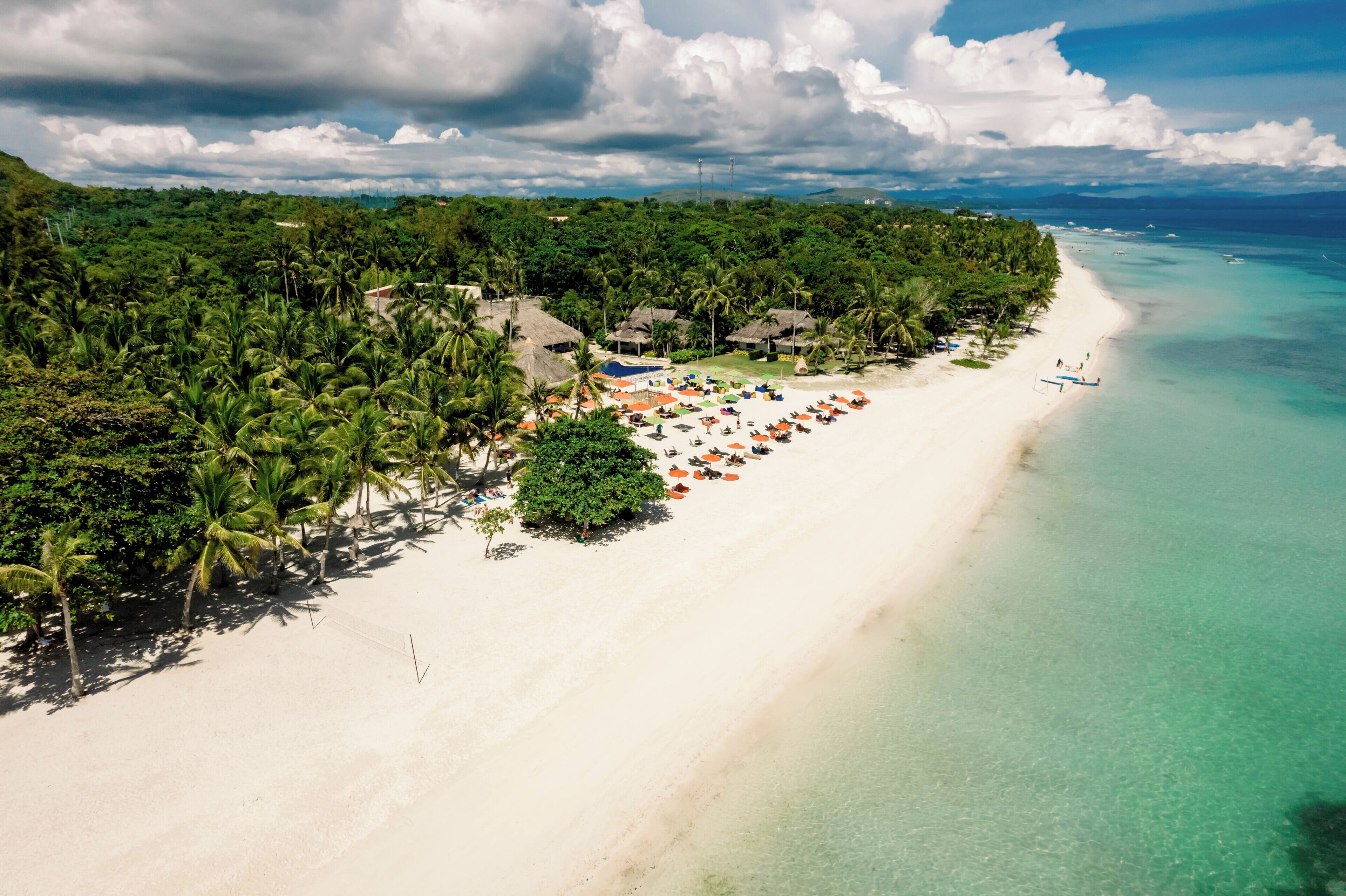 A tropical beach resort with a long sandy beach, palm trees, and a clear blue sea.