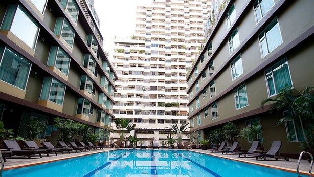 A swimming pool with lounge chairs and a tall residential building in the background. - Dynasty Grande Hotel (Bangkok)