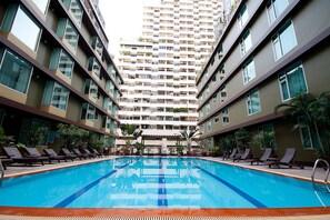 A swimming pool with lounge chairs and a tall residential building in the background. - Dynasty Grande Hotel (Bangkok)
