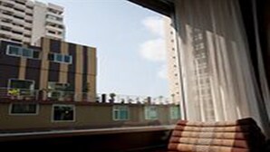 A room with a view of a high-rise building, a wooden bench, and a window with curtains. - Dynasty Grande Hotel (Bangkok)