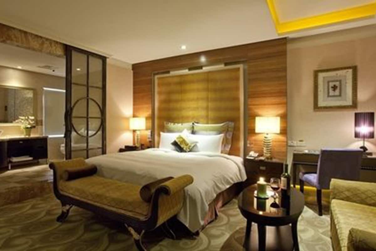 Quarto de hotel com uma cama grande, um espaço de estar com uma poltrona, uma escrivaninha e um espelho.