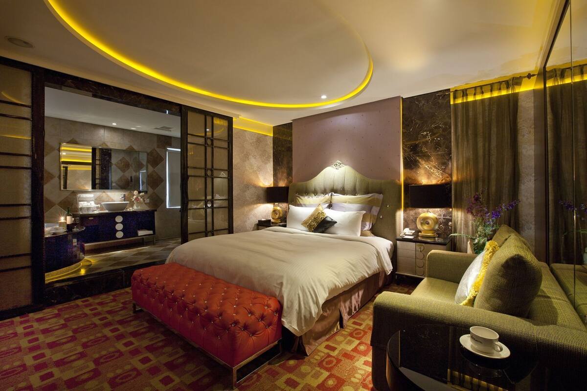 Quarto de hotel moderno com uma cama grande, área de estar, toucador com espelho e vista para a cidade.