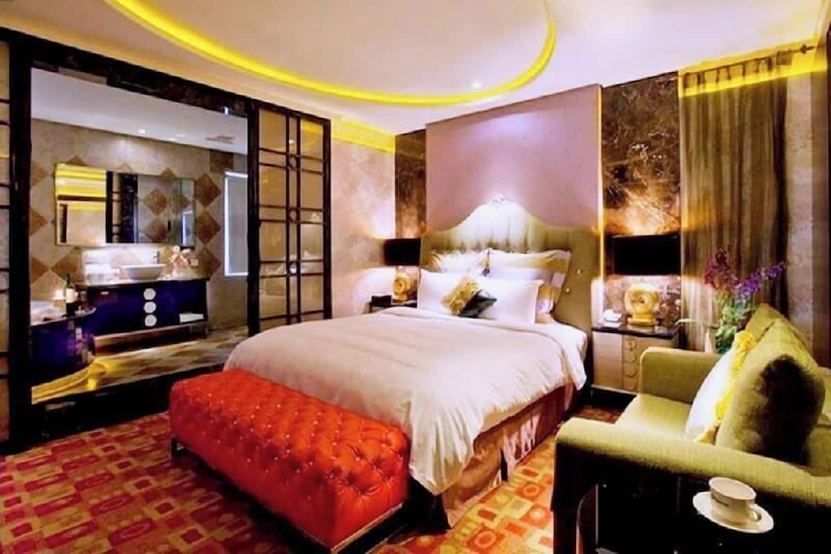 Quarto de hotel com uma cama grande, um banquinho vermelho, um sofá, uma mesinha com uma xícara e um espelho.