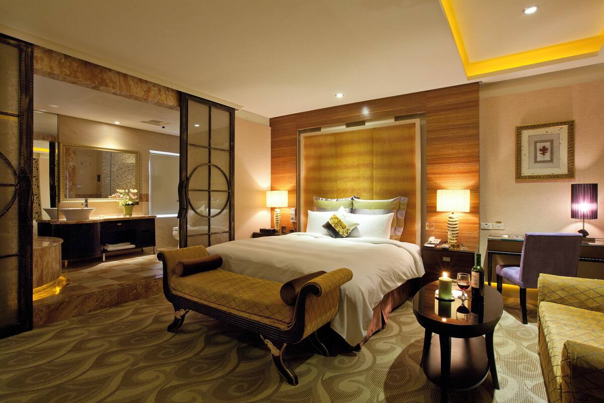Quarto de hotel com cama, escrivaninha, cadeira, sofá, mesa com vela e espelho.