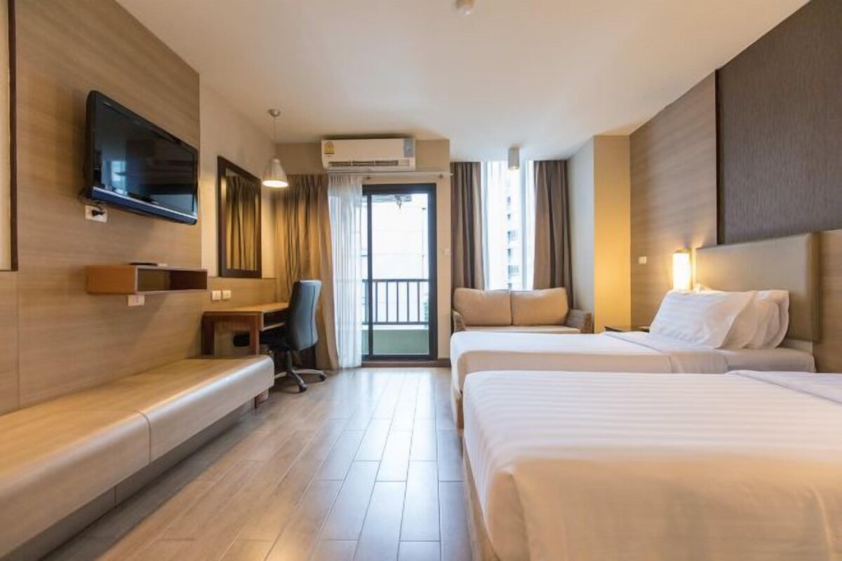 A hotel room with a bed, a desk, a chair, a television, and a balcony.