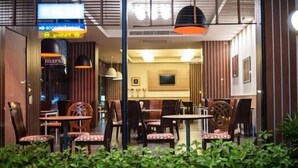 An indoor dining area with tables and chairs, a TV mounted on the wall, and a sign above the entrance. - Marsi Hotel (Bangkok)