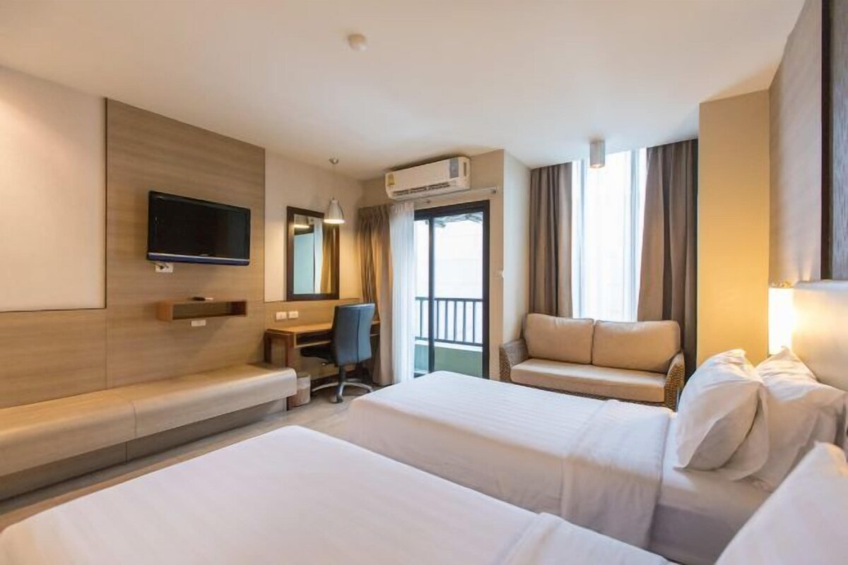 A hotel room with two beds, a desk, a chair, a TV, and an air conditioning unit.