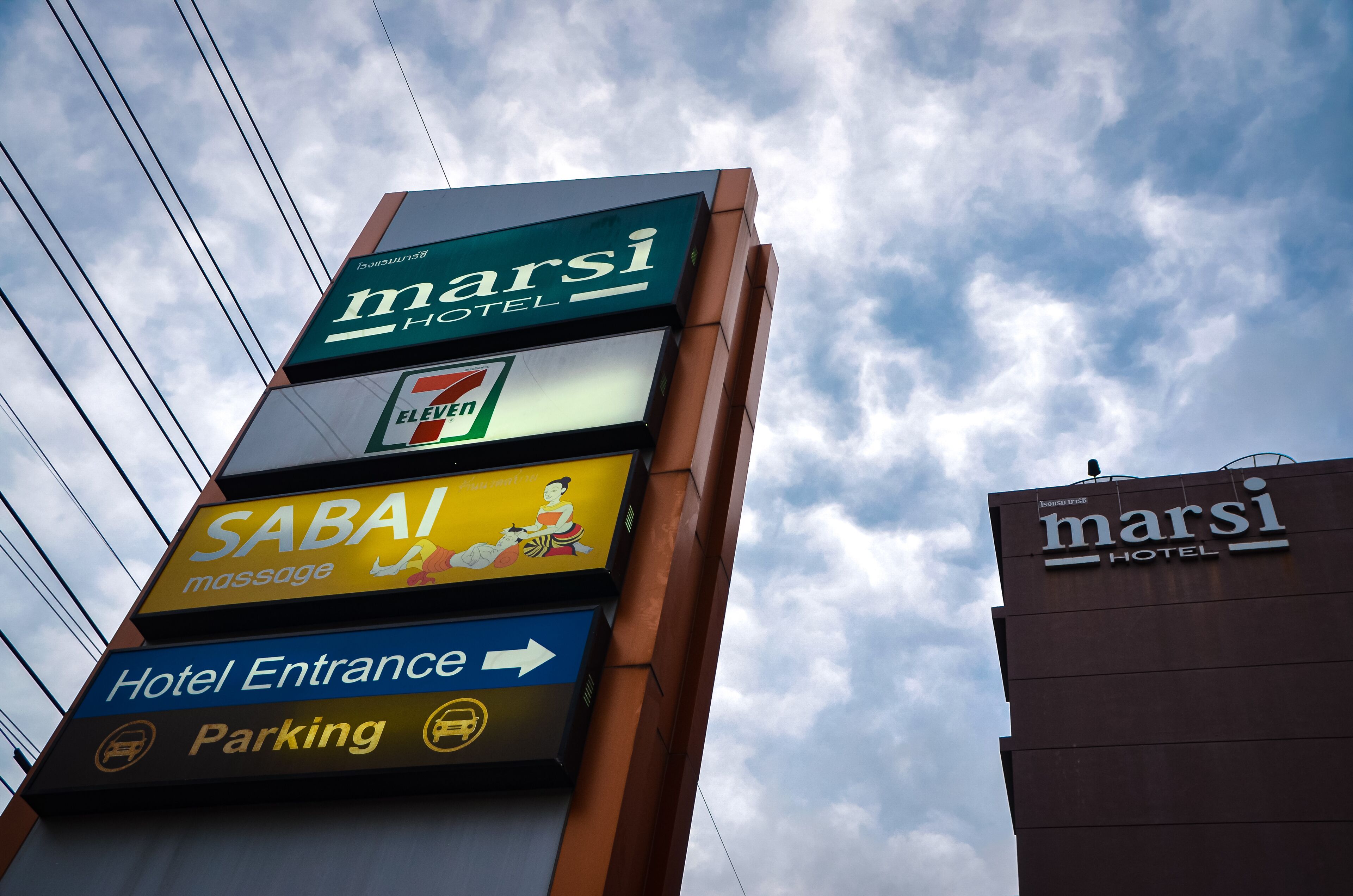 Ein Hotelschild mit verschiedenen Annehmlichkeiten, darunter ein 7-Eleven, Massageservices sowie eine Wegbeschreibung zum Hoteleingang und zum Parkplatz.
