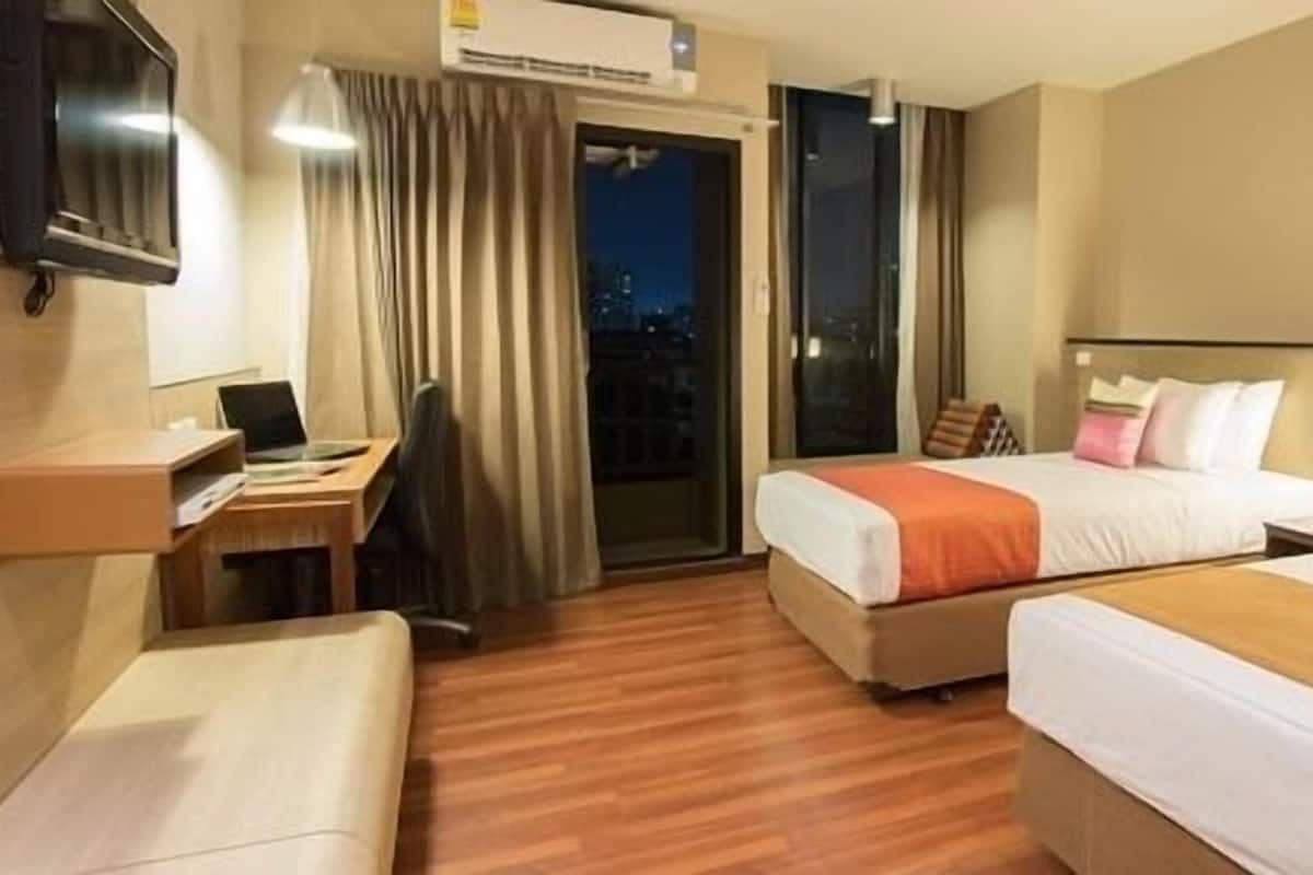 A hotel room with two beds, a desk, a chair, and a TV.