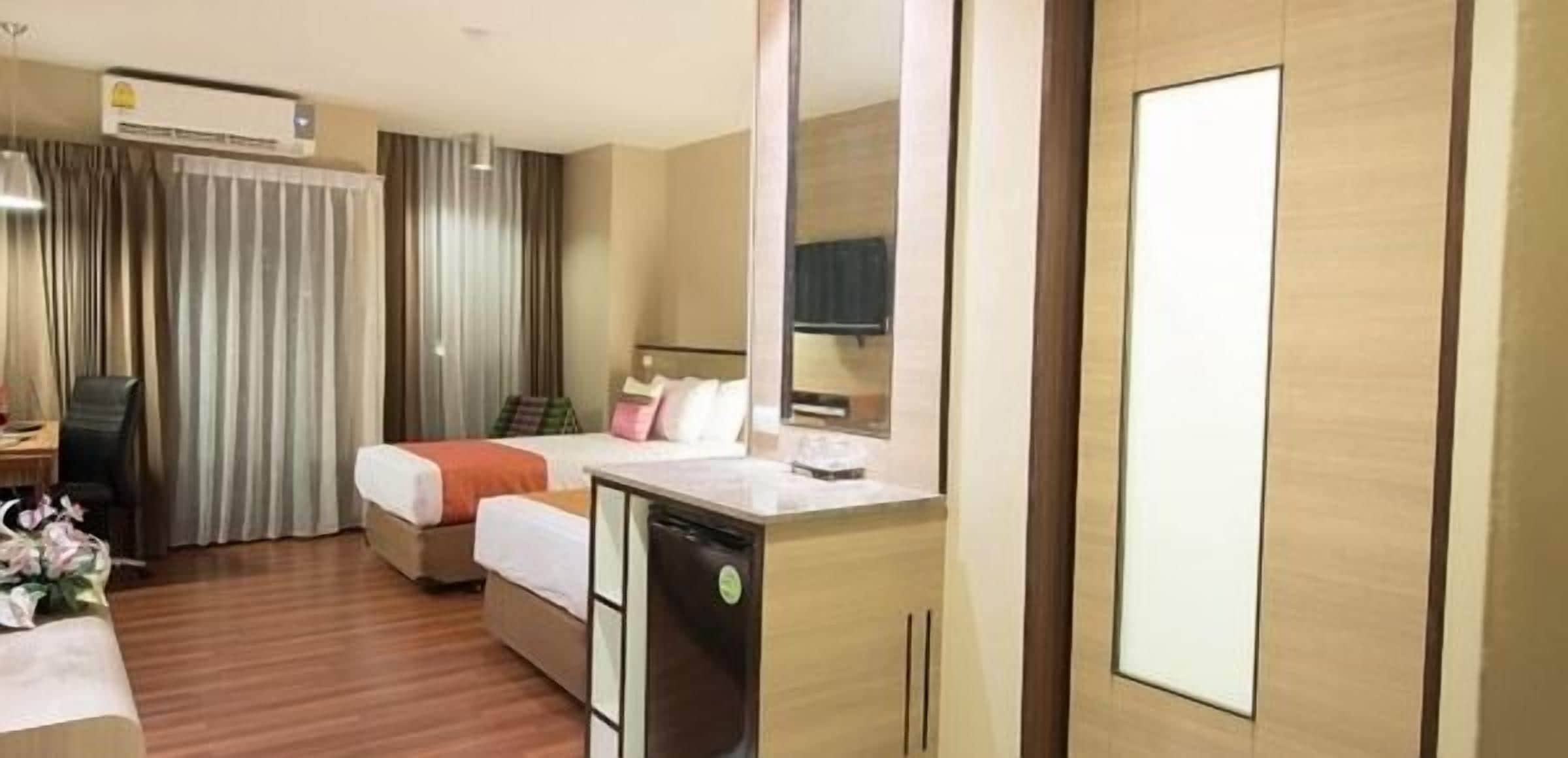 A hotel room with a bed, a desk, a small kitchenette, and a mirror.