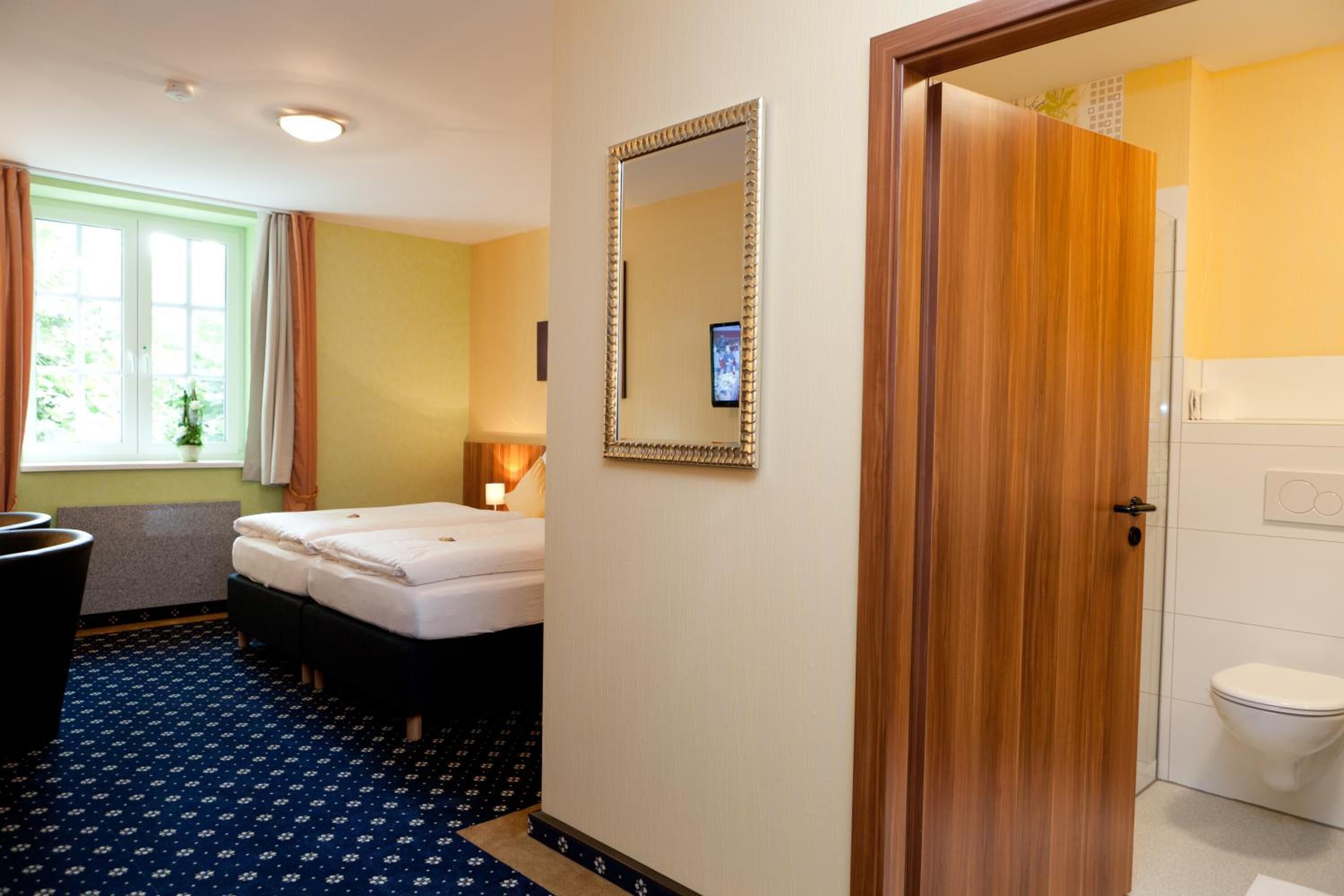 Habitación de hotel con cama doble, puerta de madera, espejo y baño con inodoro.