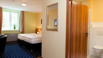Habitación de hotel con cama doble, puerta de madera, espejo y baño con inodoro.
