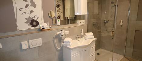A modern bathroom with a glass-enclosed shower, a white sink with a mirror above, and a floral-patterned wall.