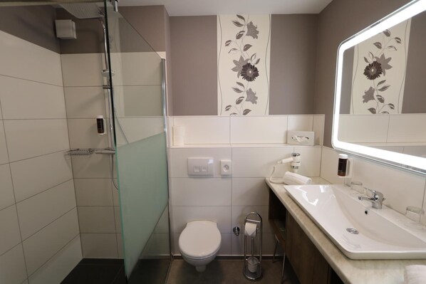 A bathroom with a glass shower enclosure, a toilet, and a sink with a mirror.