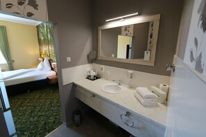 Un baño de hotel con un espejo grande, dos lavamanos, un perchero para toallas y un cubo de basura.