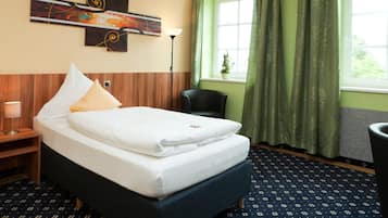 A hotel room with a bed, a chair, a lamp, a painting on the wall, and a window with curtains.