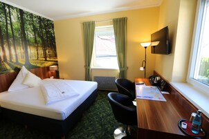 Habitación de hotel con cama, escritorio, silla y un ventanal con cortinas.