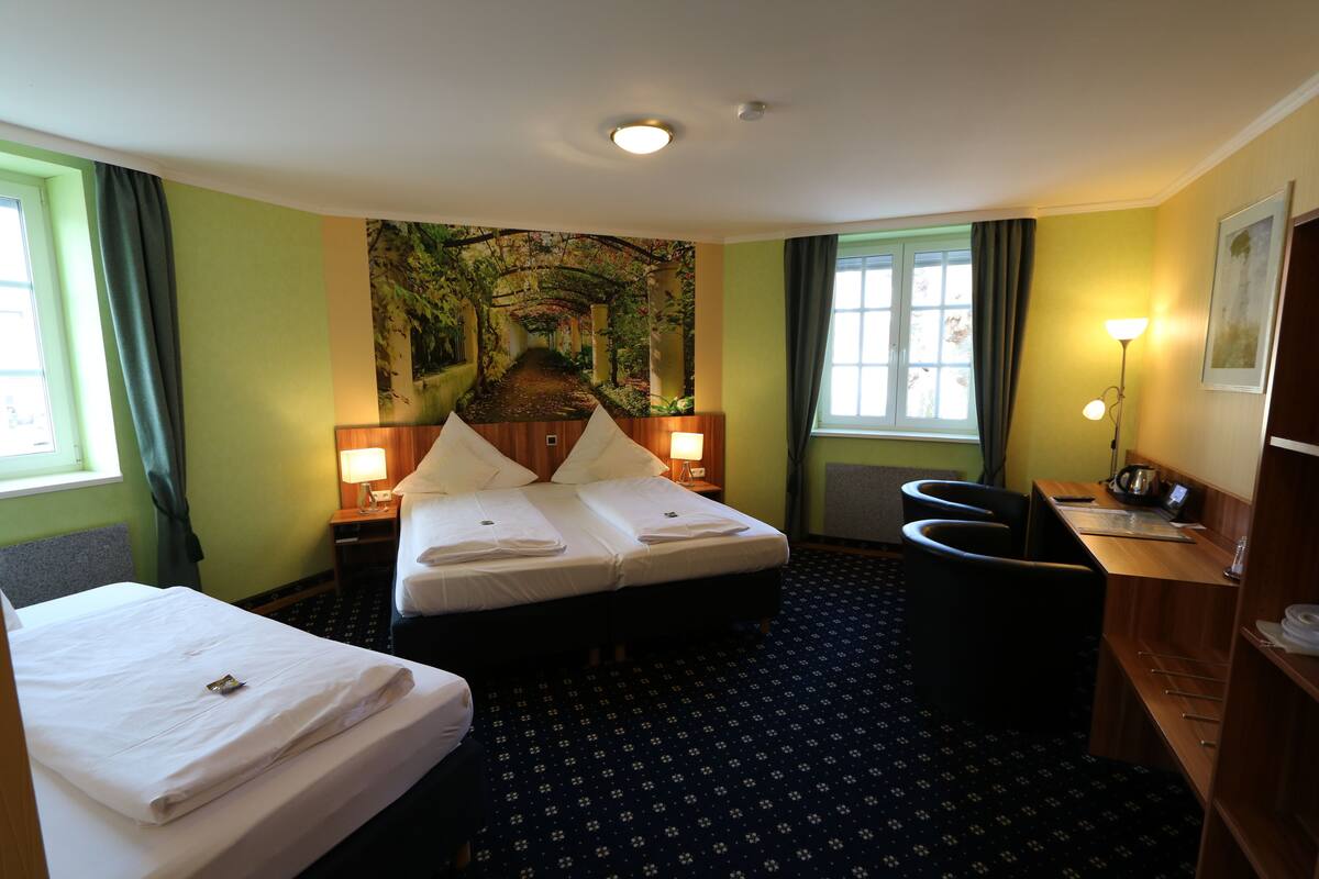 Habitación de hotel con cama, escritorio, silla, lámpara y un mural grande en la pared.