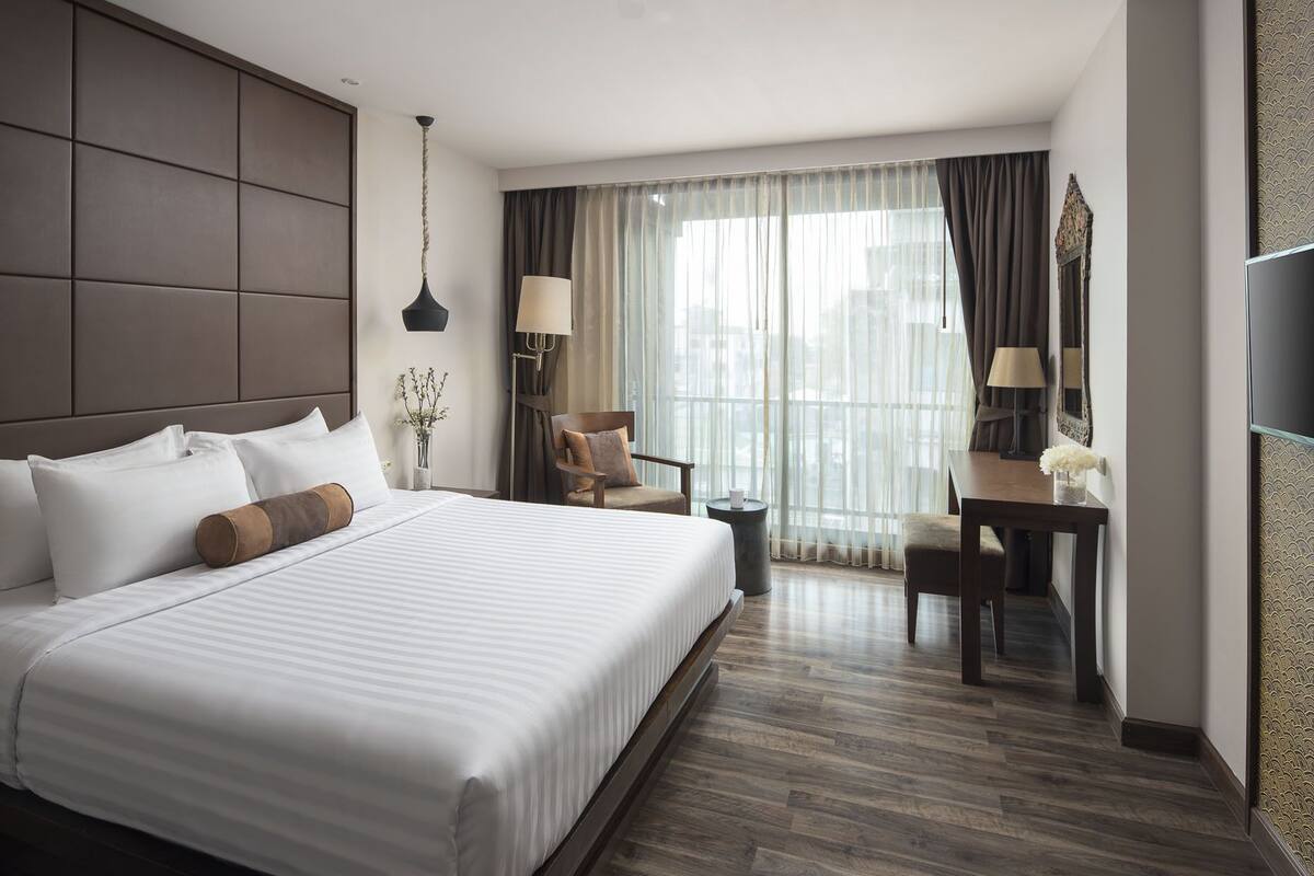 Quarto de hotel com cama grande, escrivaninha, cadeira, televisão e janela com cortinas.