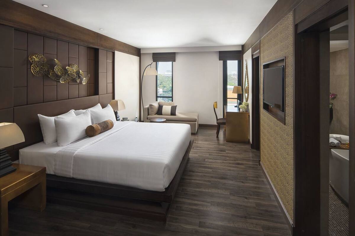 Quarto de hotel moderno com uma cama grande, um sofá, uma escrivaninha e uma televisão.