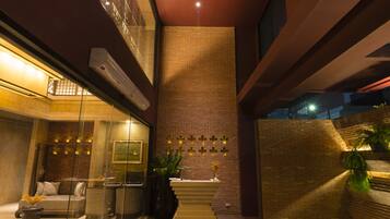 A modern lobby with a glass partition, a seating area, a staircase, and a decorative wall with a geometric light fixture.