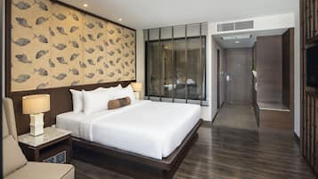 A modern hotel room with a large bed, a nightstand, a lamp, a wall with a fish pattern, a large window with blinds, and a door leading to another room.