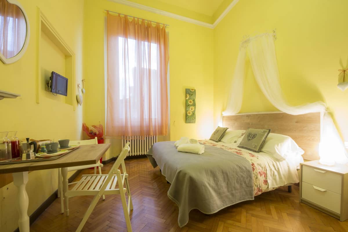 A room with a bed, bedside table, and a desk with a chair.