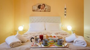 Un llit ben fet amb un estovat floral, dues làmpades laterals i un carro de servei per al matí amb te, cafè i pa.