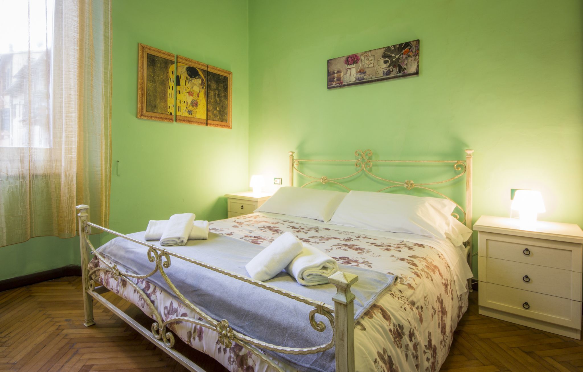 Una cama con ropa de cama floral, dos mesitas de noche y un cuadro en la pared.