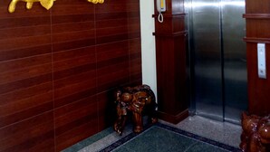 A lobby with a wooden wall featuring golden decorative elements, a reception desk, and a modern elevator. - 79 Living Hotel (Mandalay)