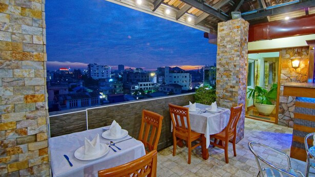 An outdoor dining area with tables and chairs, a stone pillar, and a view of a cityscape at dusk. - 79 Living Hotel (Mandalay)