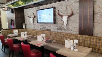 A restaurant interior with stone walls, wooden tables, red chairs, and a menu board.