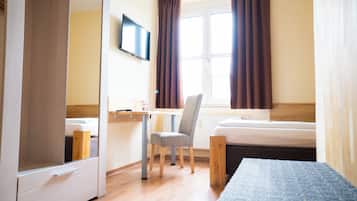 Quarto de hotel com cama, escrivaninha, cadeira, televisão e janela com cortinas.