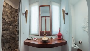 Une salle de bain avec un mur en pierre, un meuble-lavabo en bois, un miroir, une fenêtre et des toilettes.