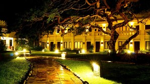 A well-lit pathway leading to a building with multiple doors and windows, surrounded by trees and illuminated by ground lights. - Areindmar Hotel (Nyaung-U)