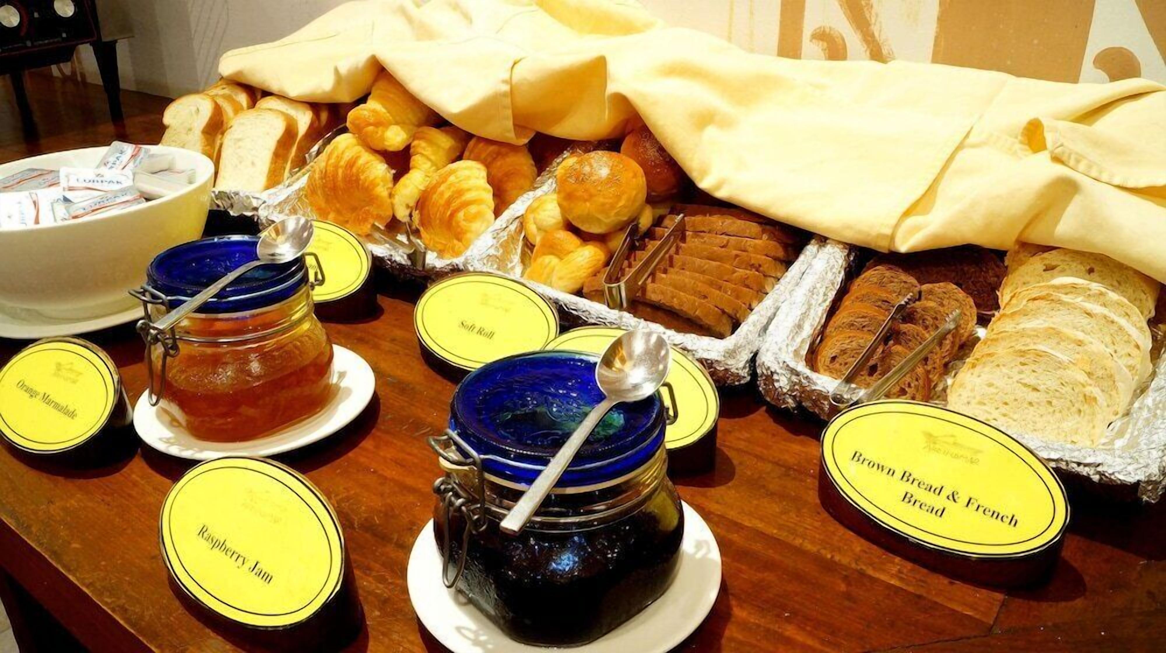 A breakfast buffet with labeled jars of jam, bread, and pastries.