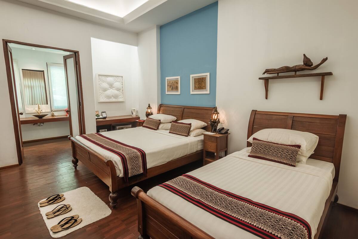 Ein Hotelzimmer mit zwei hölzernen Betten, einem großen Spiegel, einer blauen Wand als Akzent und einem Holzregal mit Dekoration.