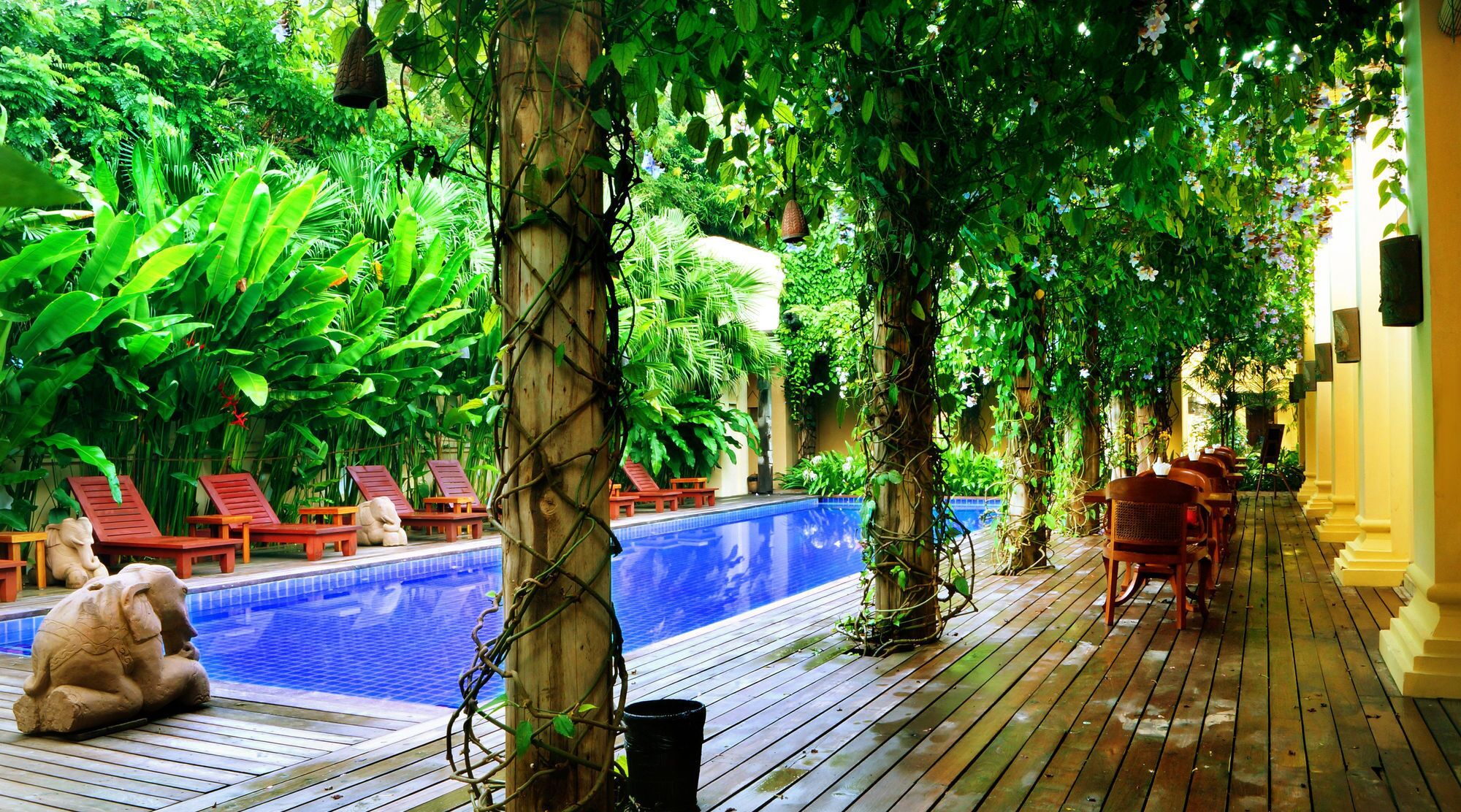 Zona de piscina con terraza de madera, sillas de descanso y una estatua.