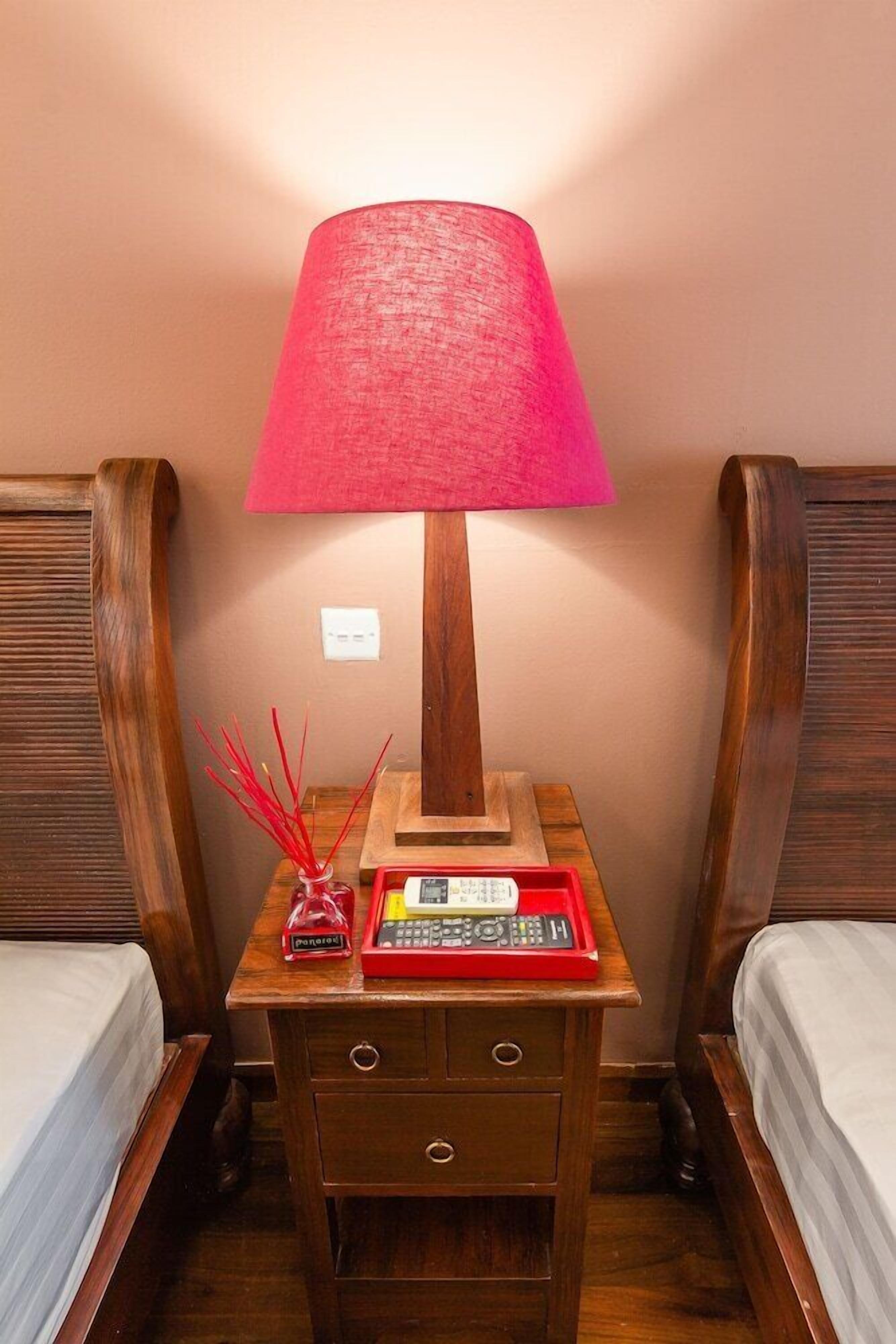 A wooden nightstand with a red lamp, a red telephone, and a small vase with red sticks.
